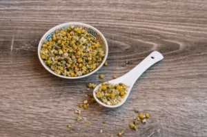 Un cucchiaio ed un piatto di ceramica che contengono i fiori di camomilla essiccata